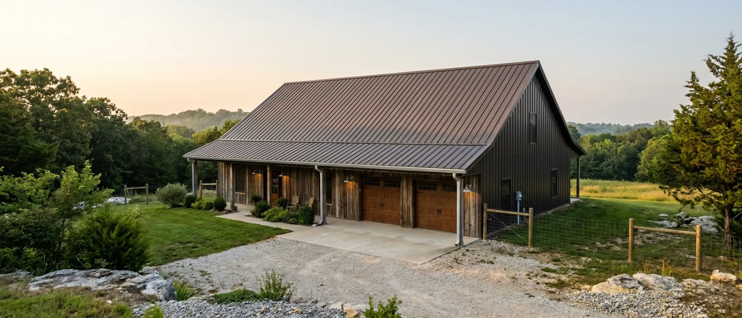 A completed barndominium viewed from a low angle showing its standing seam metal roof, vertical wall panels, gutters and exterior wall lights.