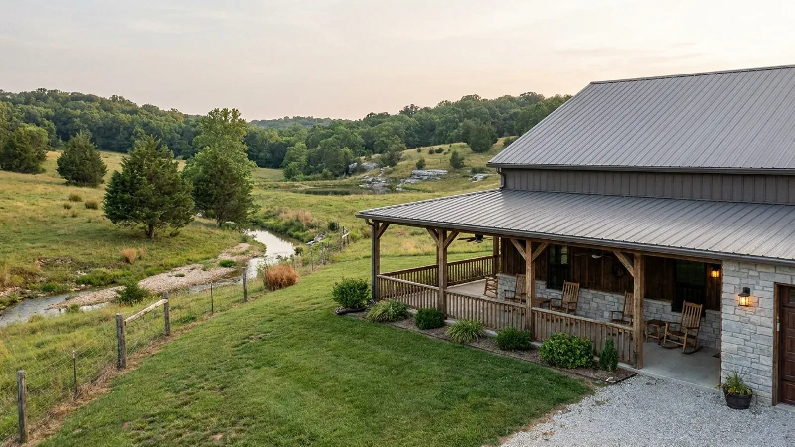 A barndominium exterior showing a deep wrap-around covered porch with posts and railing along two sides of the building.
