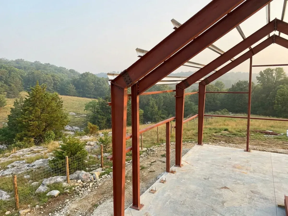 A red oxide primed structural steel frame partly erected on a concrete slab, showing bolted knee joints and anchor bolts.
